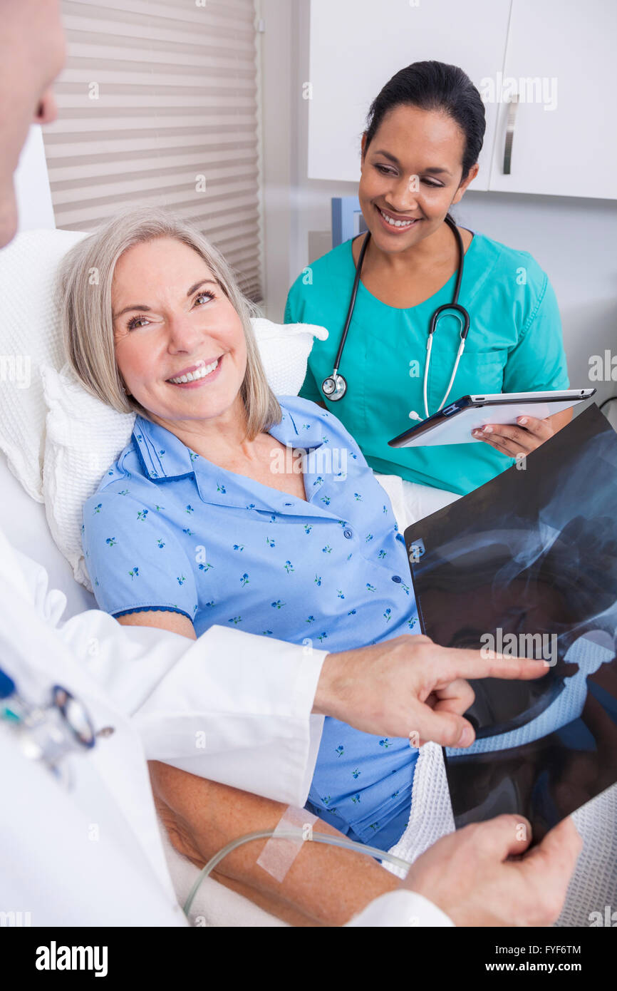 Un felice senior donna femmina paziente anziano a letto guardando a raggi X di un'anca sostituzione con connettore maschio di tipo medico e ispanica Foto Stock