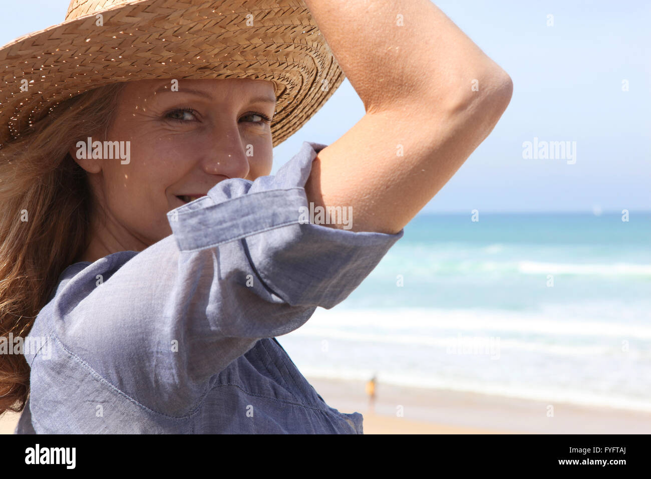 Donna che mantiene sul suo cappello di paglia in una brezza Foto Stock