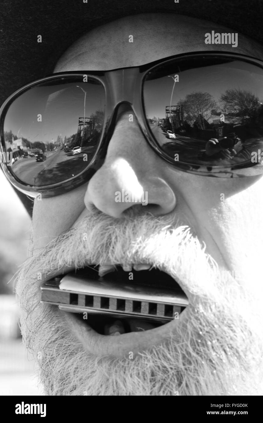 Senzatetto uomo che indossa sfumature mette un armonica a bocca Foto Stock