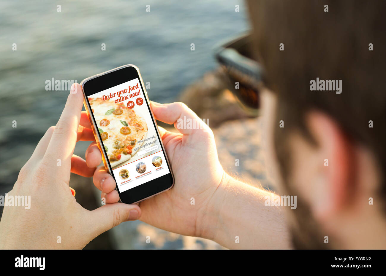 L uomo sulla costa, utilizzando il suo smartphone per ordinare la pizza online. Tutti i grafici dello schermo sono costituiti. Foto Stock