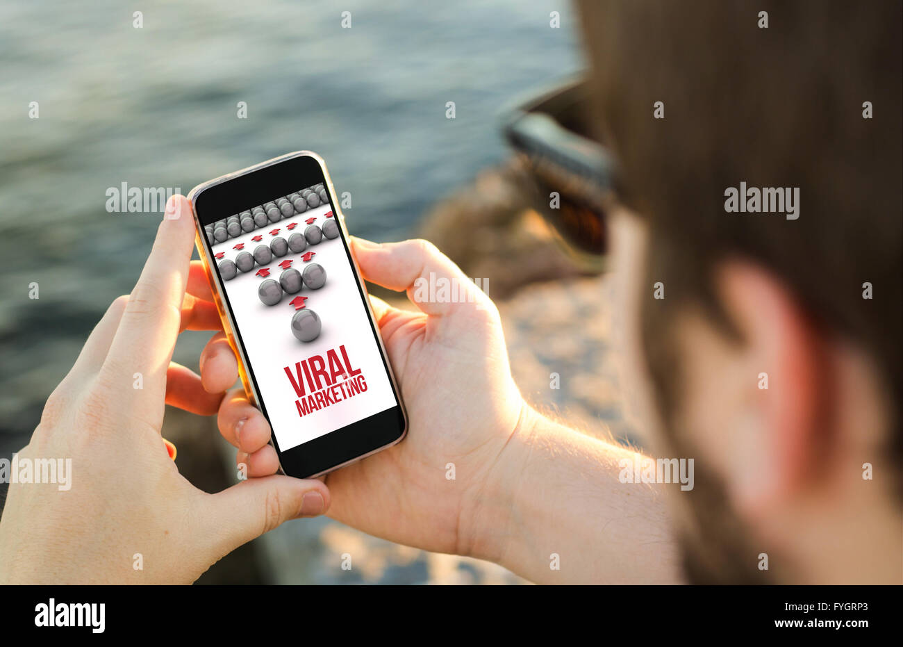 L uomo sulla costa, utilizzando il suo smartphone che mostra il marketing virale concetto. Tutti i grafici dello schermo sono costituiti. Foto Stock