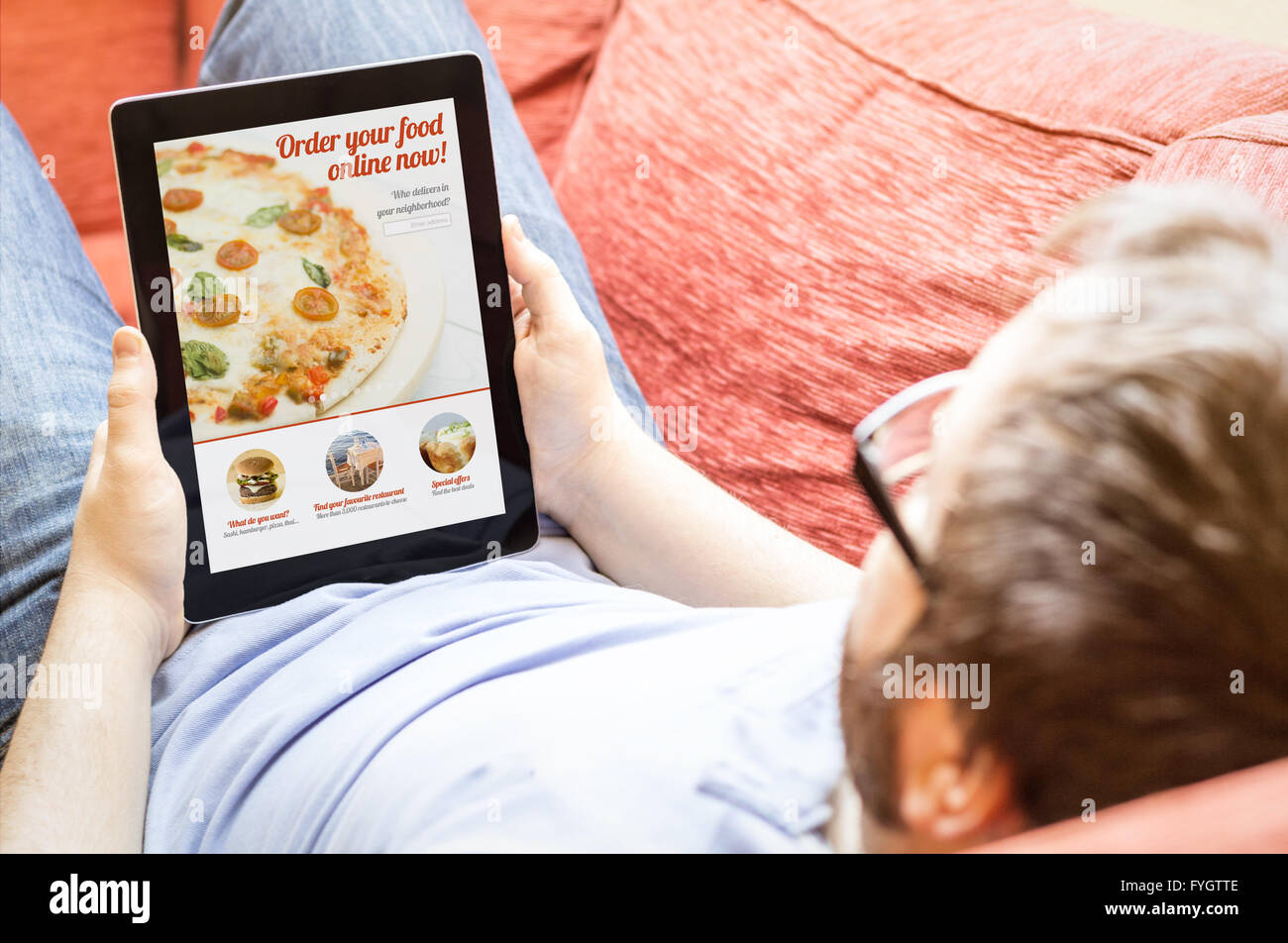 Tecnologia il concetto di stile di vita: hipster uomo a ordinare una pizza su un tablet al divano. Tutti i grafici dello schermo sono costituiti. Foto Stock