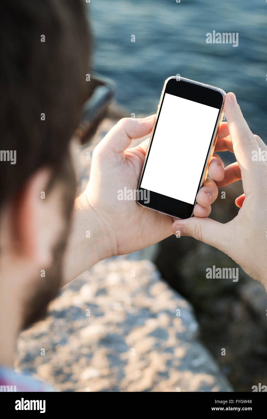 Uomo con occhiali da sole con uno schermo vuoto smartphone vicino al mare Foto Stock