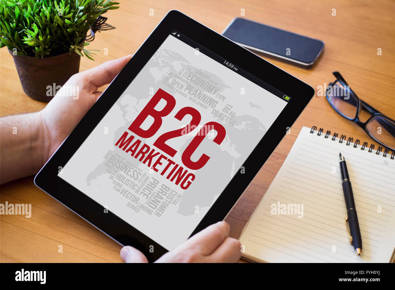 Le mani di un uomo con una b2c concetto dispositivo su di un area di lavoro in legno tavolo. Tutti i grafici dello schermo sono costituiti. Foto Stock
