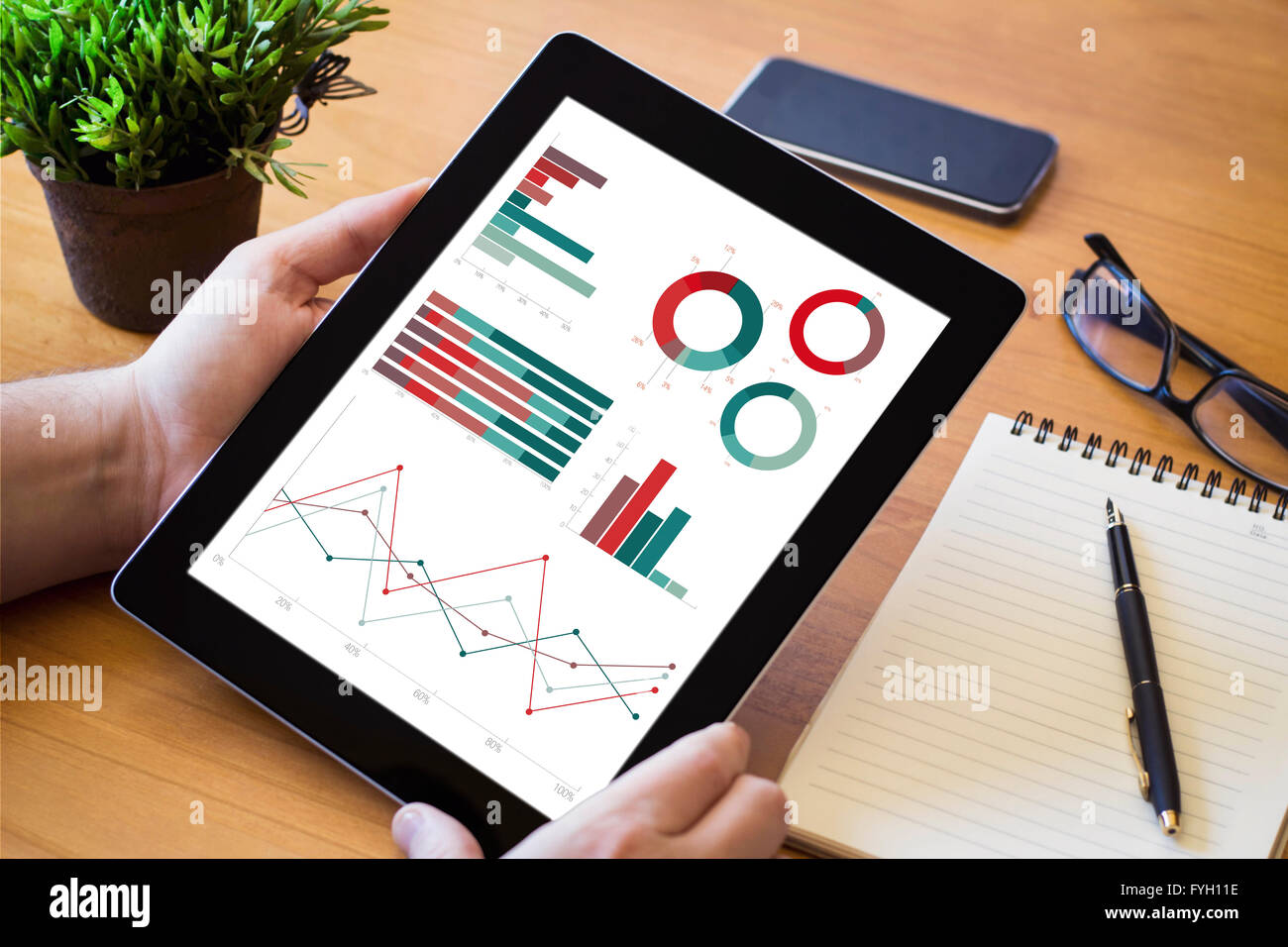 Le mani di un uomo con una pianificazione finanziaria dispositivo su di un area di lavoro in legno tavolo. Tutti i grafici dello schermo sono costituiti. Foto Stock