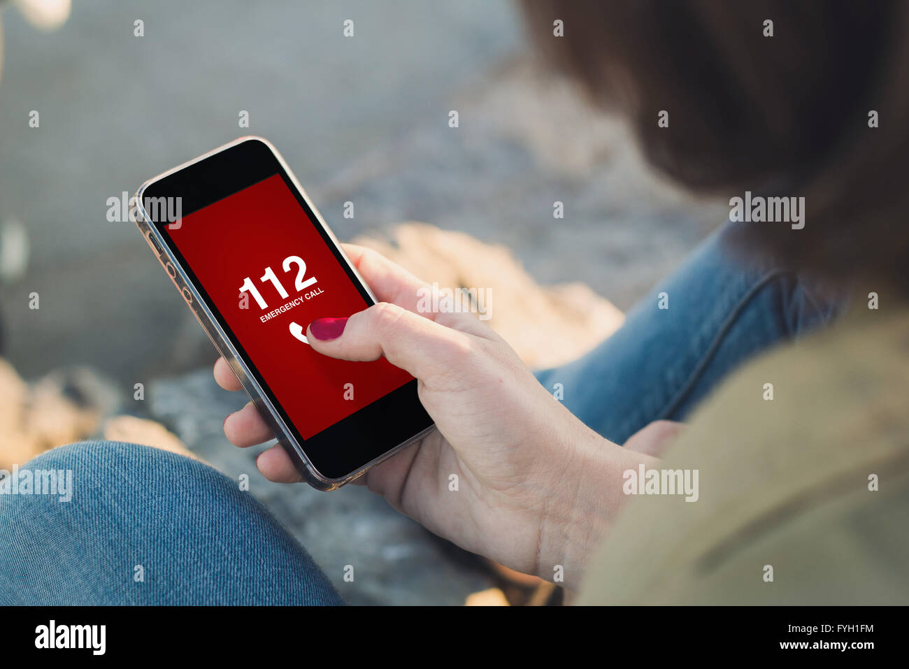 Donna che mantiene uno smartphone di comporre il numero di emergenza sullo schermo. Tutti i grafici dello schermo sono costituiti. Foto Stock