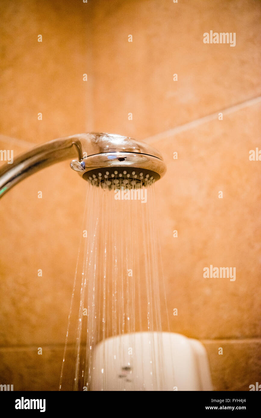 Il vapore e il calore che sale fino ad un massimale di luce da una doccia cromo in testa in una piccola piastrelle doccia interna Foto Stock