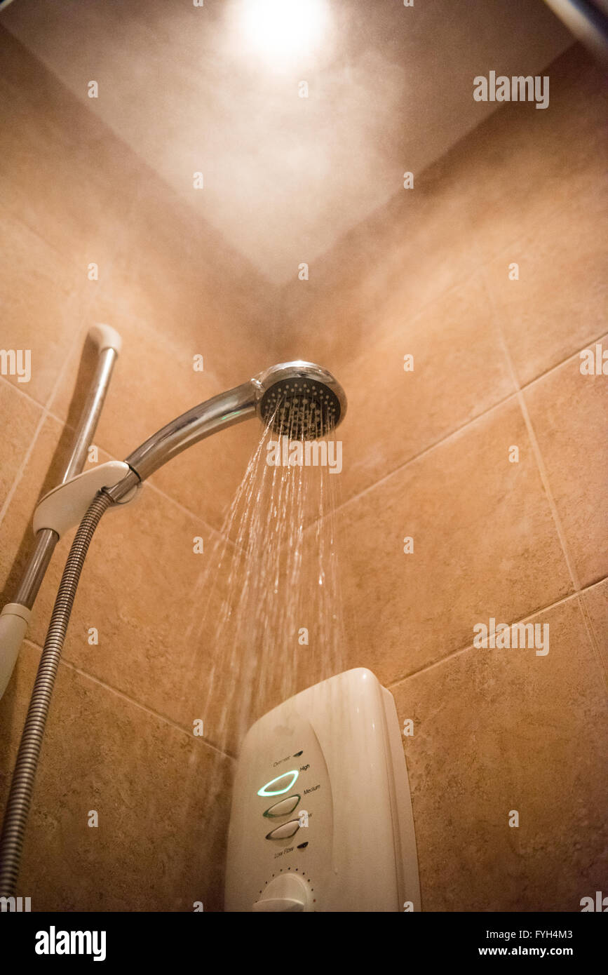 Il vapore e il calore che sale fino ad un massimale di luce da una doccia cromo in testa in una piccola piastrelle doccia interna Foto Stock