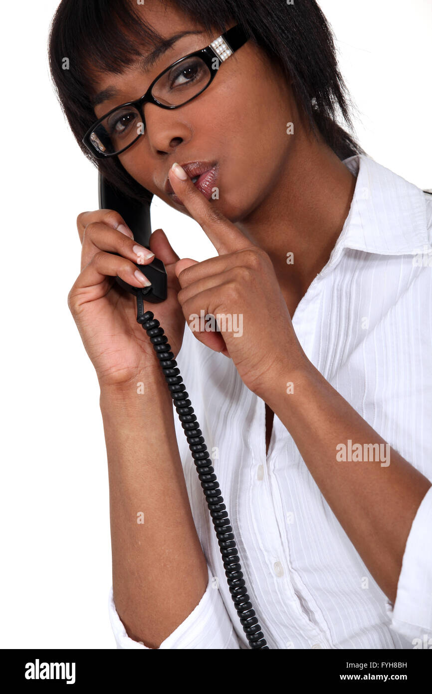 Donna al telefono facendo un segno di silenzio Foto Stock