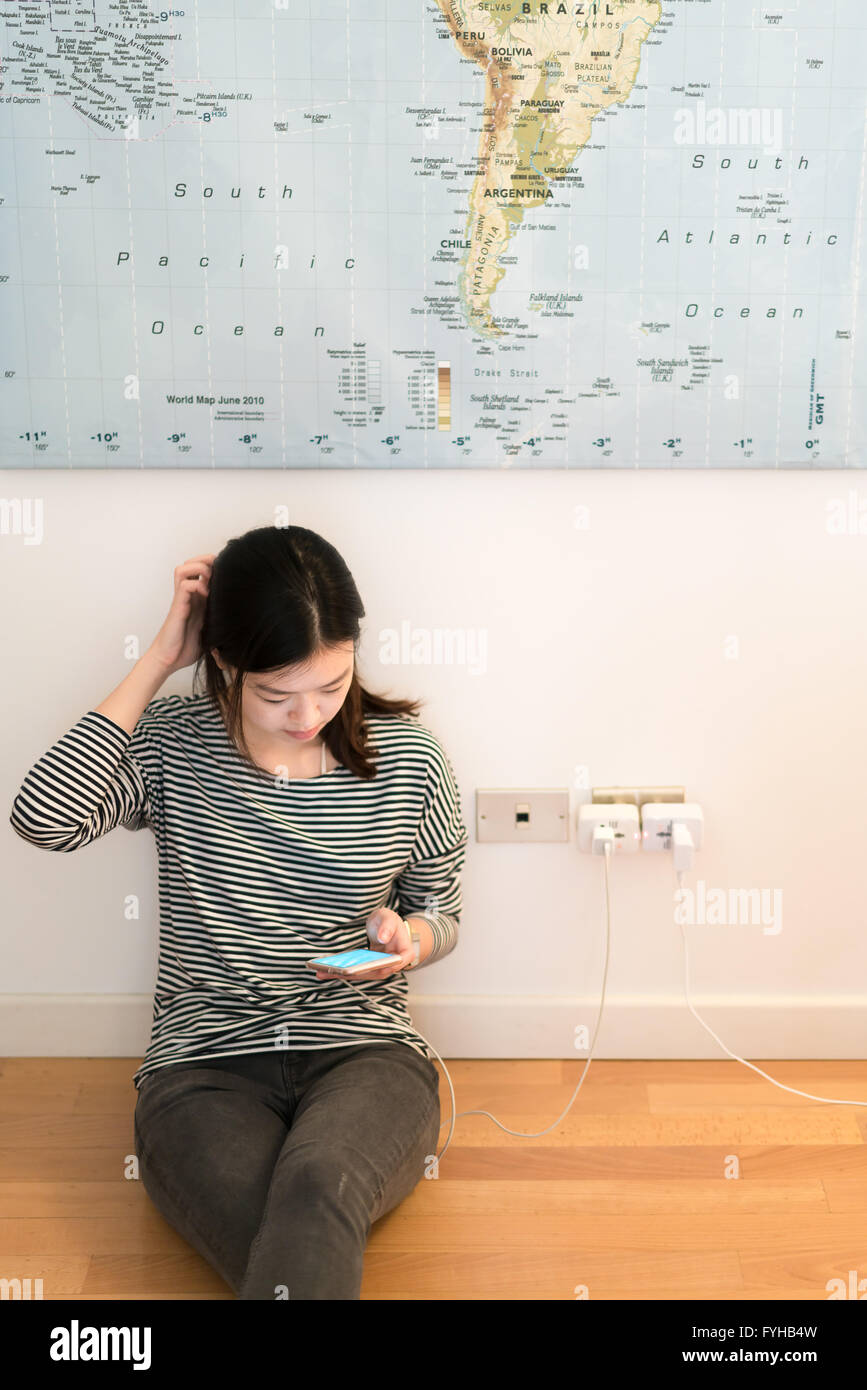 Carino ragazza asiatica frustrante con la batteria del telefono, la carica sulla parete Foto Stock