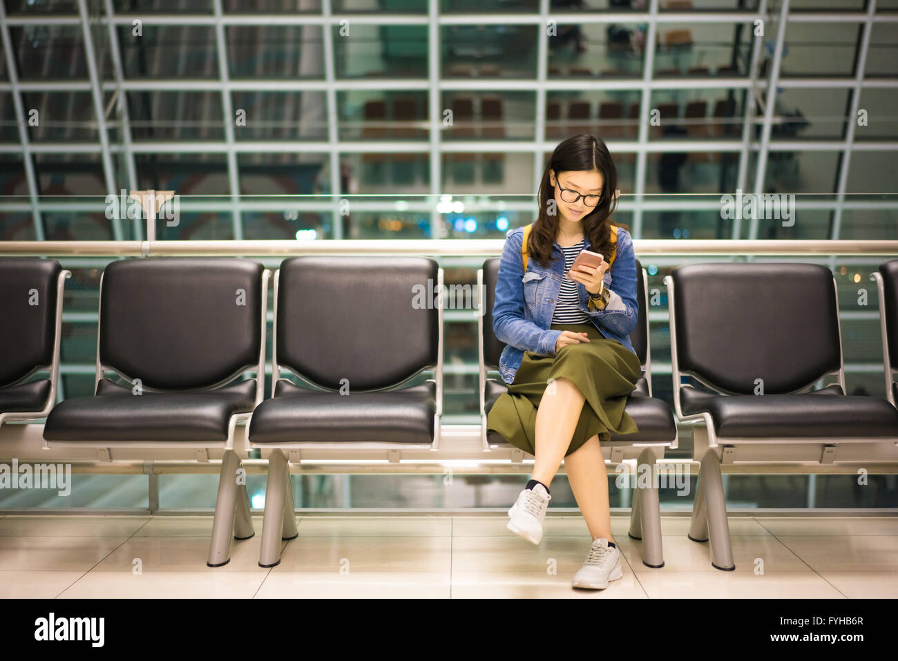 Bella ragazza asiatica seduto da solo, sorridente a smartphone, in attesa a salire a bordo del velivolo, concettuale Foto Stock