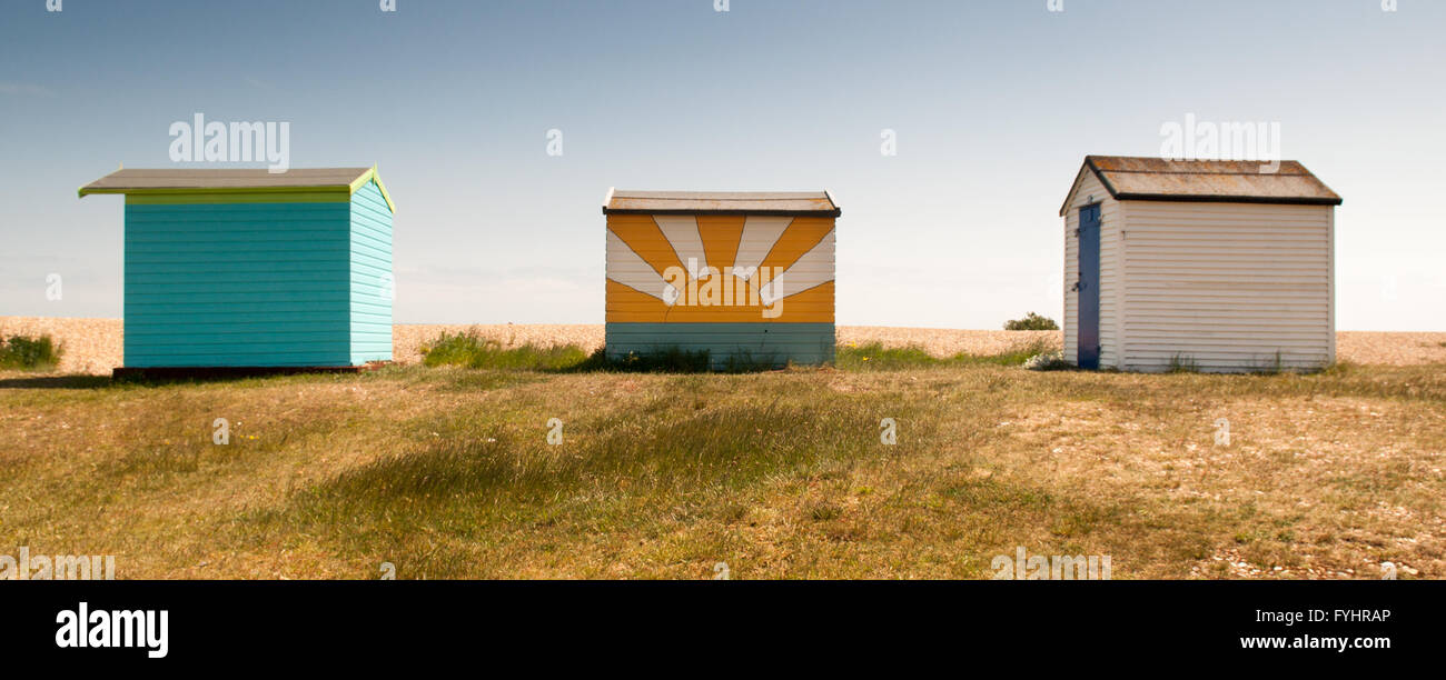 Una tripletta di cabine sulla spiaggia, a New Romney nel Kent. Uno beach hut è plainted con un murale di sun. Foto Stock