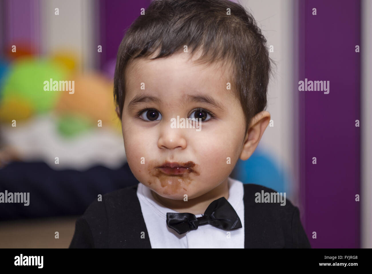 Felice, adorabile happy baby mangiando cioccolato, indossa una tuta e il filtro bow tie Foto Stock