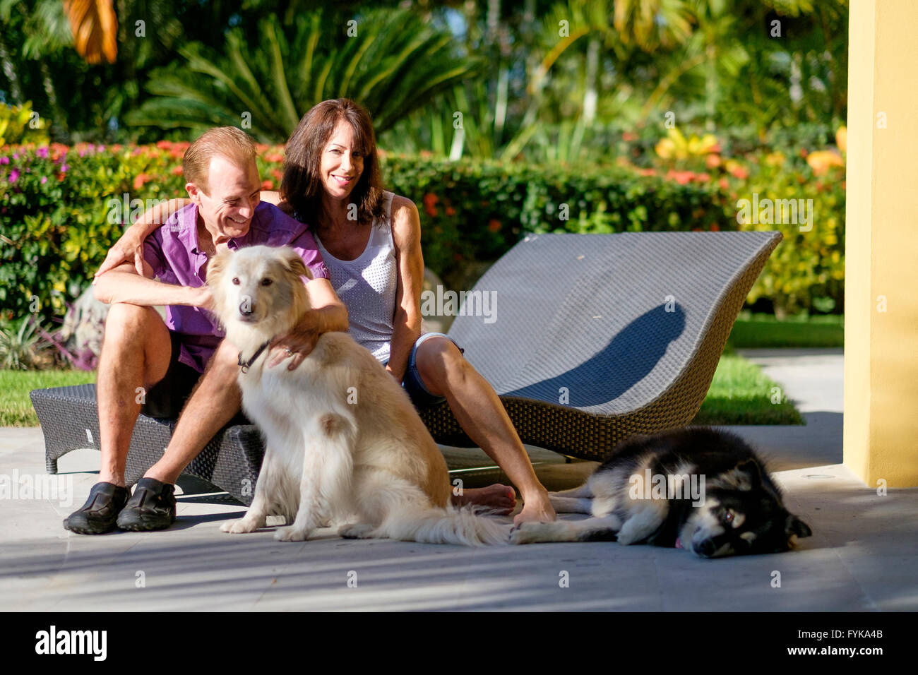 Senior pensionati l uomo e la donna come accarezzare i loro 2 cani seduti su sedie a sdraio nel giardino della loro casa in Messico Foto Stock