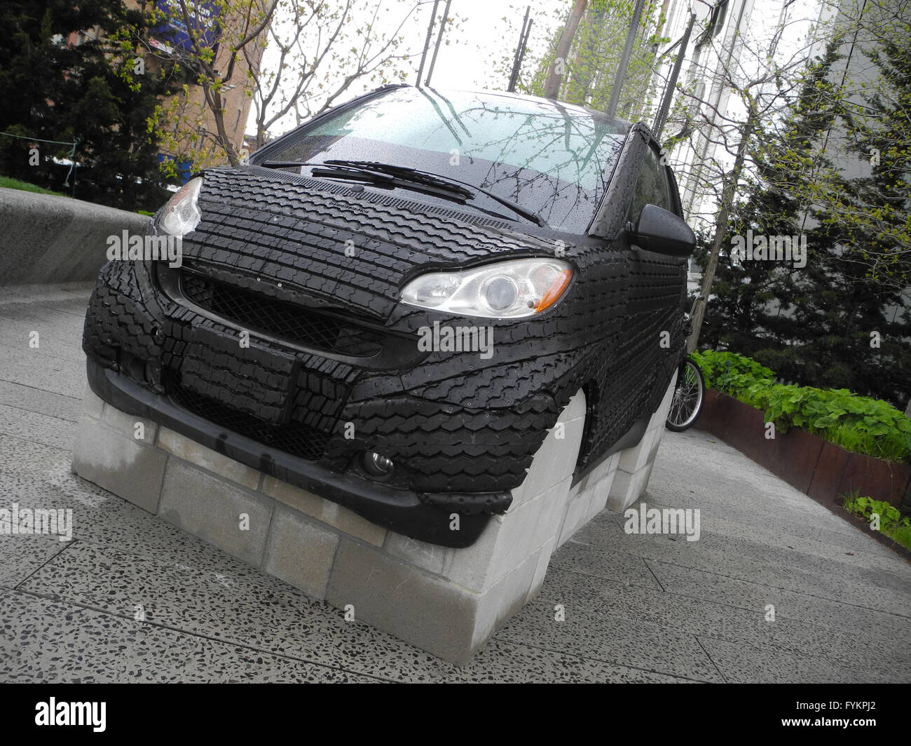 Una gomma di smart car può essere visto in New York, Stati Uniti d'America, 26 aprile 2016. La grande scultura realistica di un sonnambulismo uomo in mutande setti i visitatori in un parco di New York. Artista Tony Matelli battezzato il suo bronzo dipinto pezzo 'Sleepwalker, ' che può essere visto nella linea alta Park nel sud ovest di Manhattan.La scultura è parte della mostra gratuita 'Wanderlust, ' che tratta con i piedi, viaggiare e pellegrinaggi. Il pezzo 'Smart Tree" dall artista giamaicano Nari Ward, in cui un vecchio coperchio pneumatici la vettura compatta e una mela albero cresce dal suo tettuccio apribile, è parte della mostra. Foto: JOHANNES SC Foto Stock