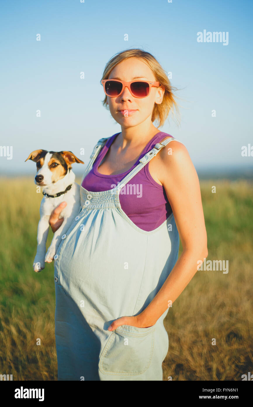 Felice donna incinta con un cane al tramonto Foto Stock