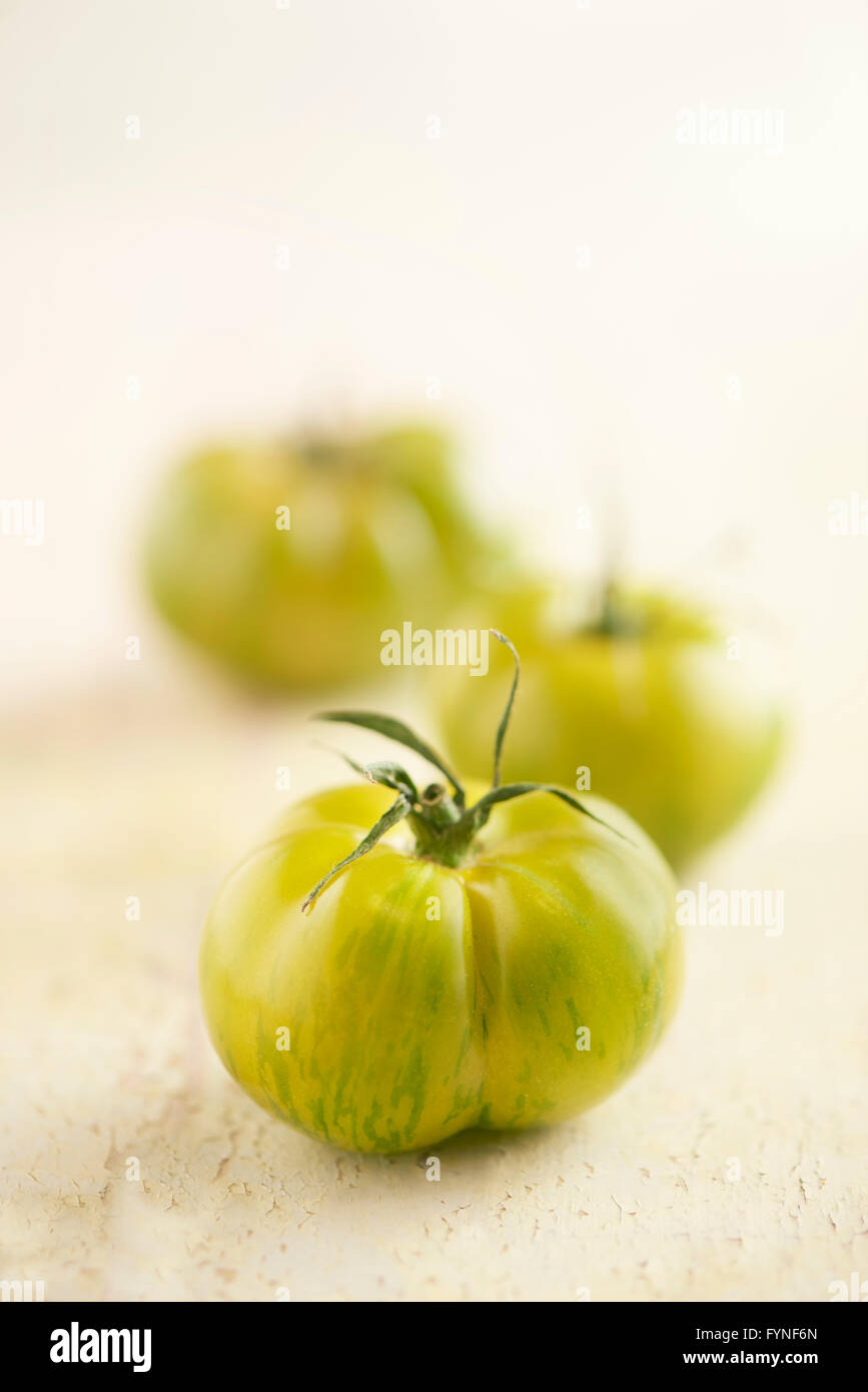 Tre verdi pomodori tiger su un sfondo di legno in una fila di recessione con particolare attenzione a quello in primo piano e copyspace sopra Foto Stock