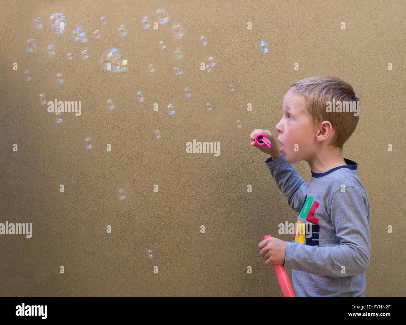 Un giovane ragazzo soffiare bolle contro un muro beige background. Foto Stock