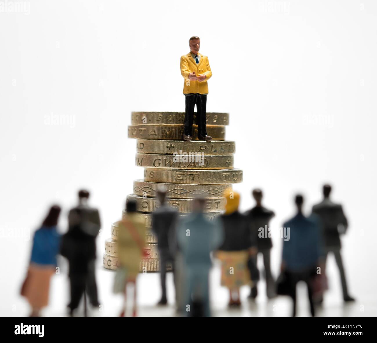 Consigli sui soldi concetto. Un imprenditore in miniatura permanente sulla sommità di una pila di una libbra di monete per parlare ad una folla di persone Foto Stock