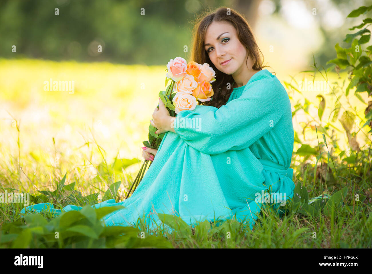 Ritratto di una giovane ragazza con un mazzo di rose seduti all'ombra degli alberi in una giornata di sole Foto Stock