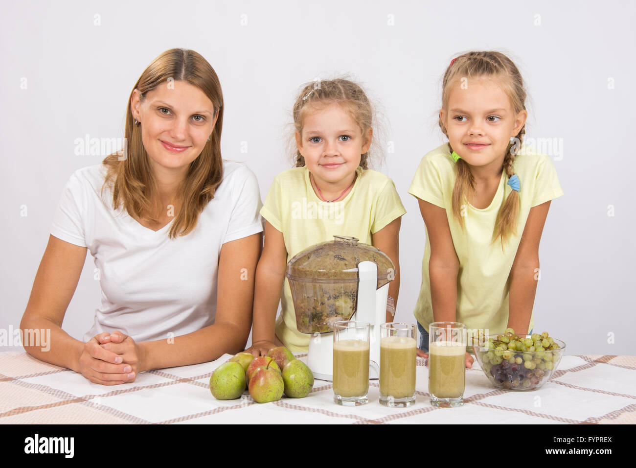 La madre e le sue due figlie per cuocere per tre bicchieri di succo centrifuga Foto Stock