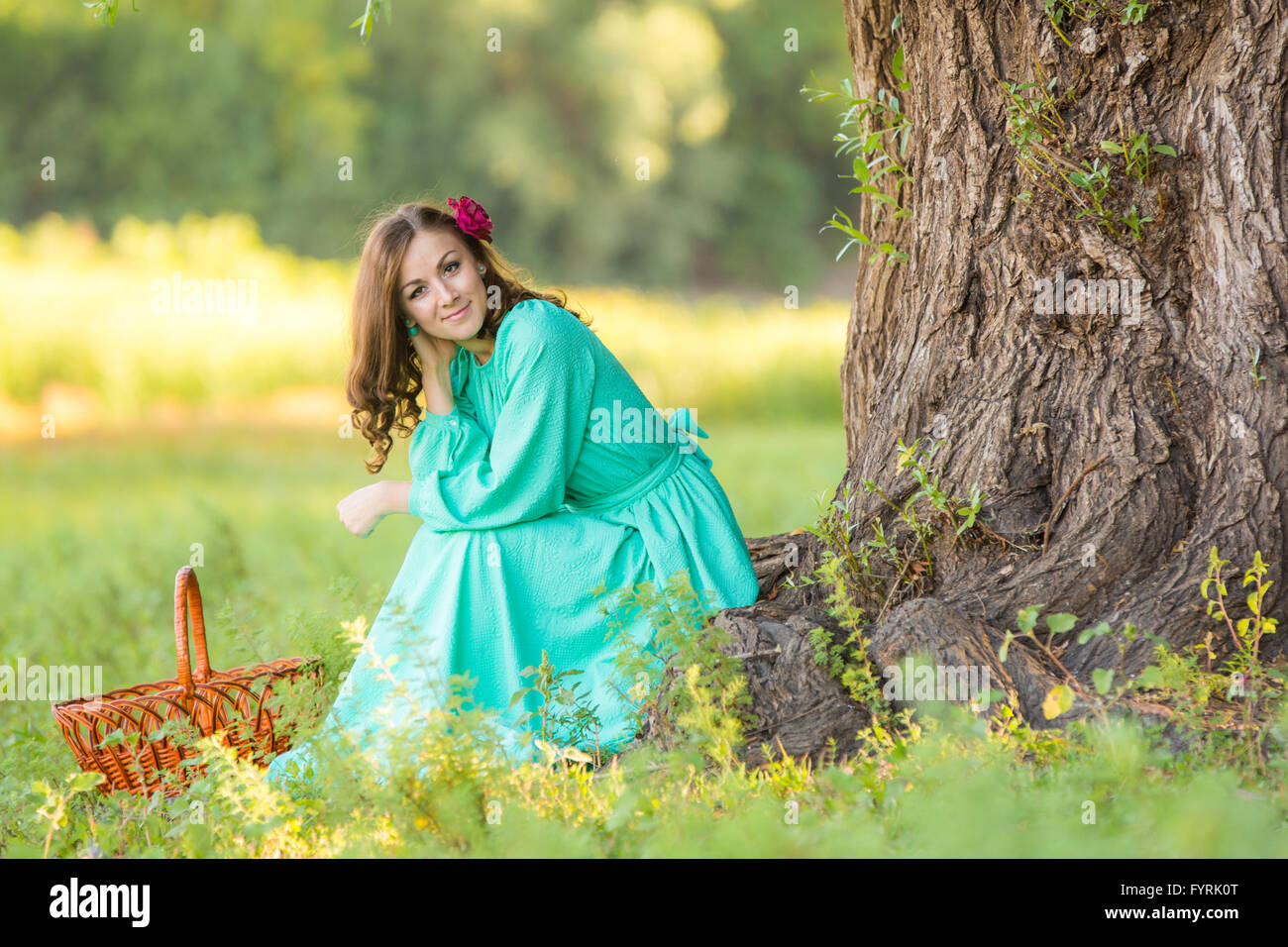 Una ragazza in un abito lungo in un buon umore rannicchiato vicino ad un albero nel bosco Foto Stock