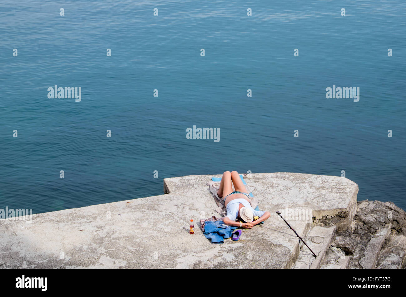 La donna a prendere il sole su una spiaggia di cemento dal mare Adriatico Foto Stock