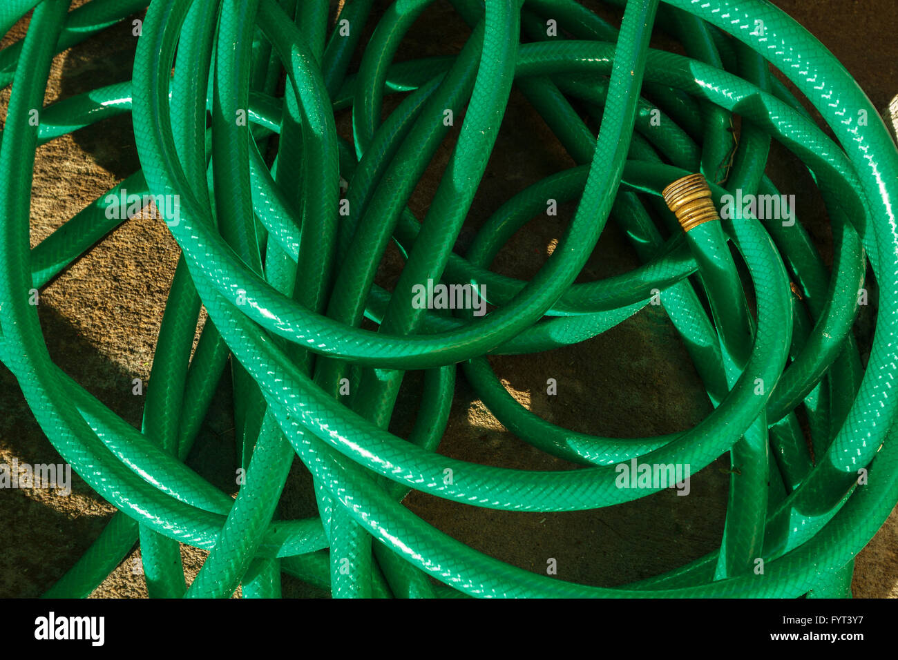 Un intricato fino pasticcio di plastica usate acqua tubo flessibile su un patio di calcestruzzo superficie su una mattina di sole. Foto Stock