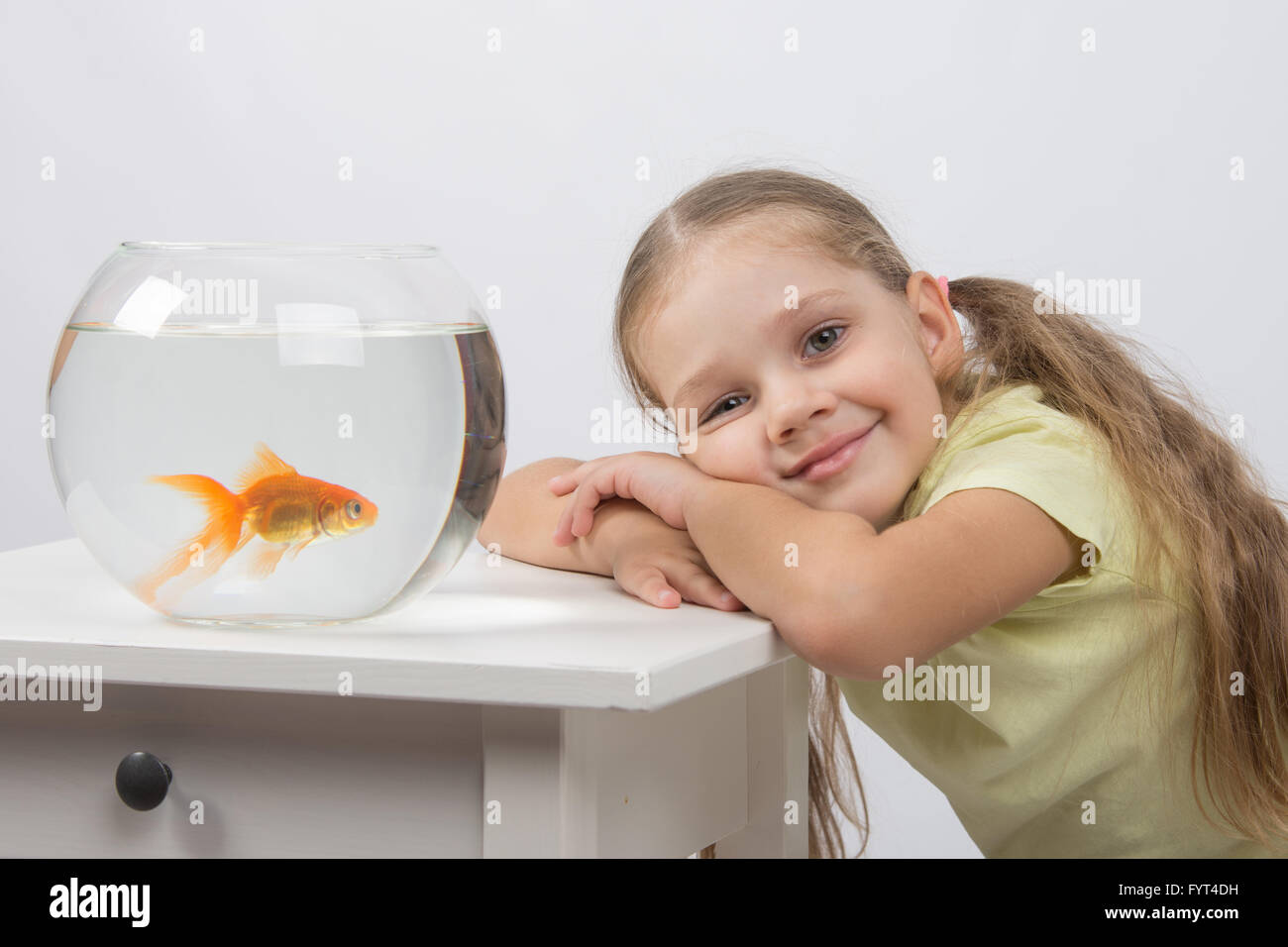 Felice di quattro anni di ragazza mettere la sua testa nelle sue mani seduto davanti a un goldfish Foto Stock