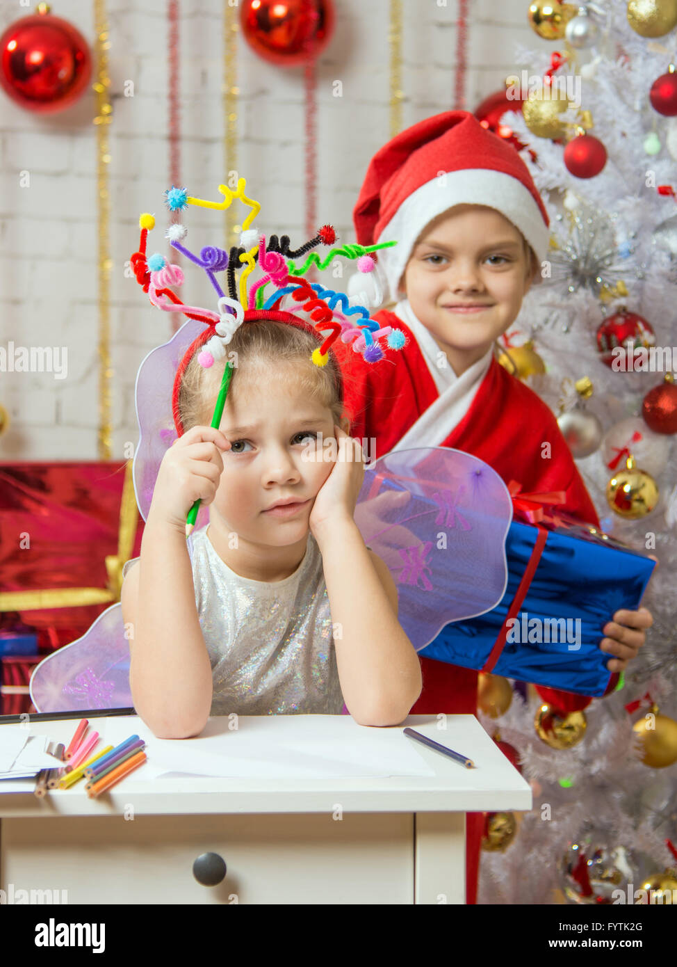 La ragazza si siede a un tavolo con i fuochi d'artificio sulla testa, santa claus il suo pronto a dare il suo dono Foto Stock