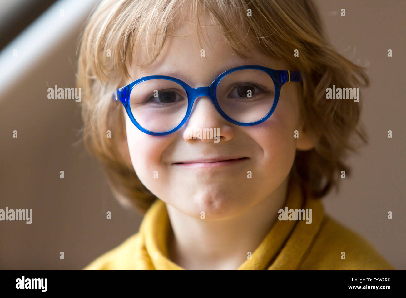 Ragazzo di 6 anni, sembra cordiale, sorrisi, con occhiali, con una cornice blu, Foto Stock