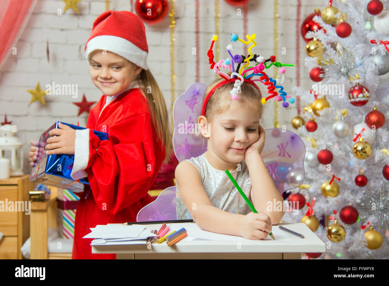 La ragazza si siede a un tavolo con i fuochi d'artificio sulla testa, Santa Claus porta il suo regalo di Natale Foto Stock