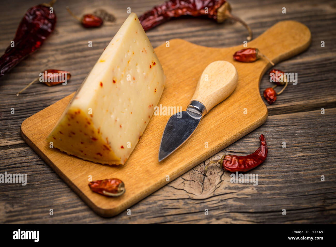Pezzo di formaggio artigianale con il peperoncino sul tagliere di legno Foto Stock