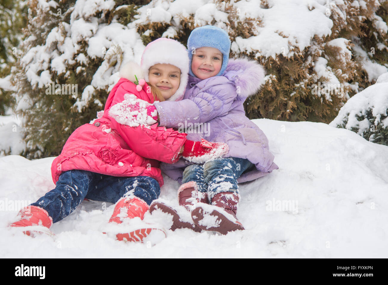 Due ragazze sono seduti in un cumulo di neve neve e abbracciando ogni altro Foto Stock