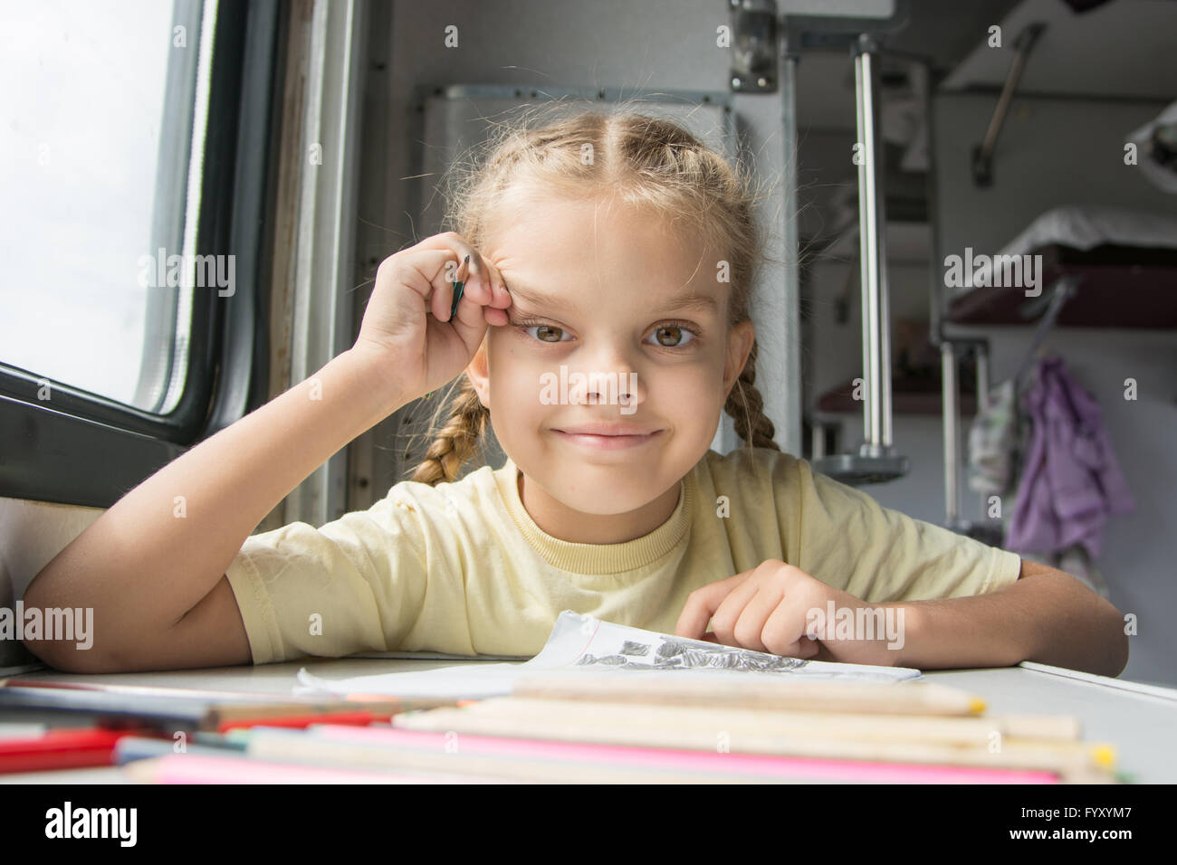 La ragazza sembra felicemente nel telaio, disegno matite in un treno Foto Stock