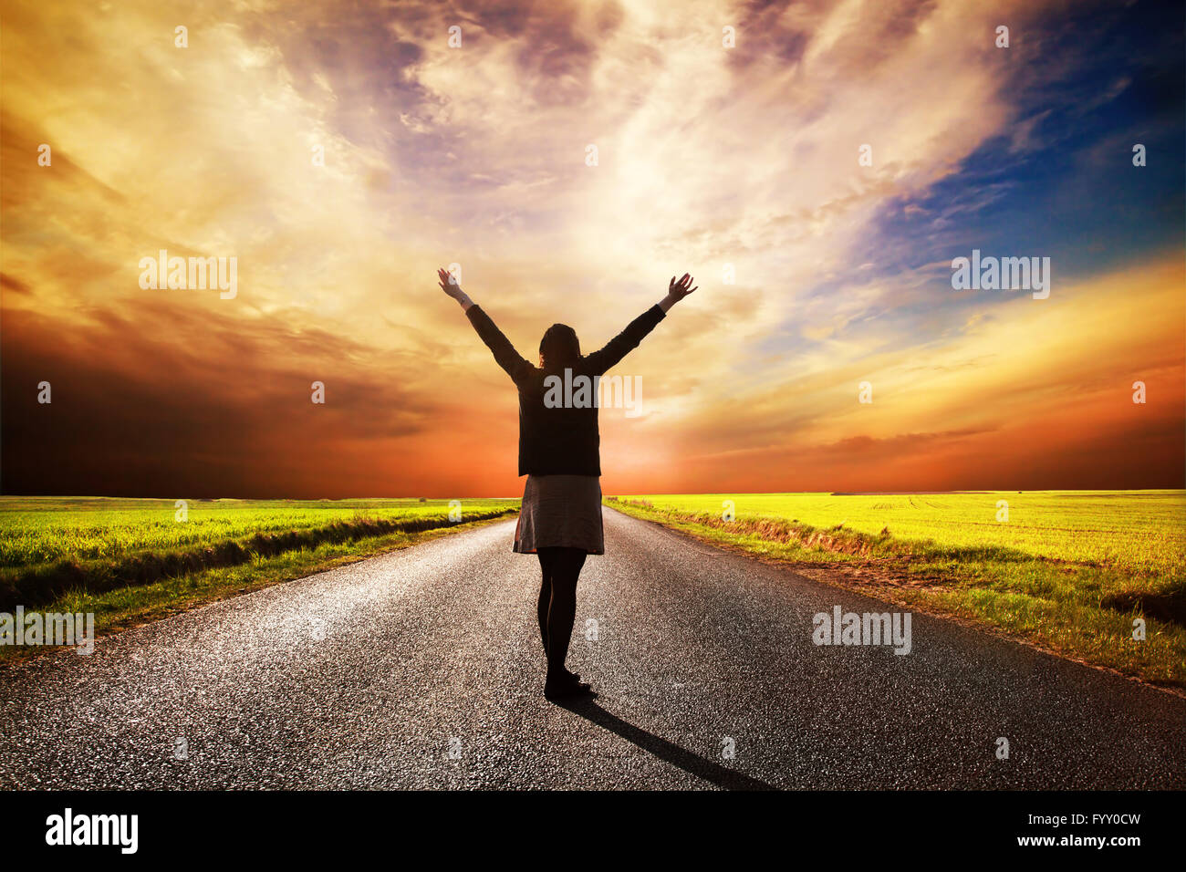 Donna felice permanente sulla lunga strada al tramonto Foto Stock