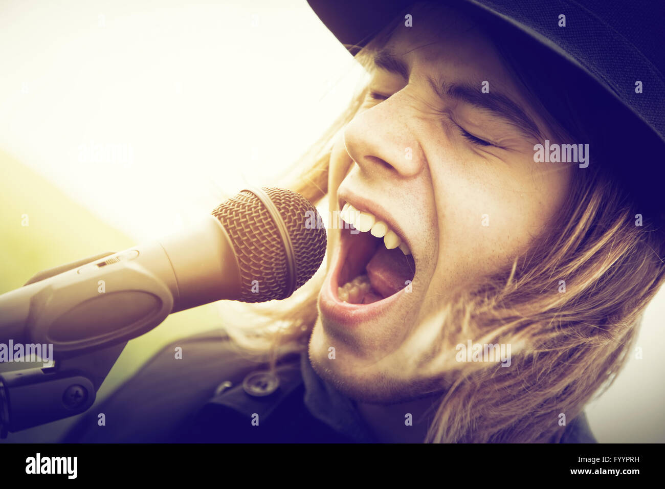 Giovane uomo con i capelli lunghi e hat cantando Foto Stock