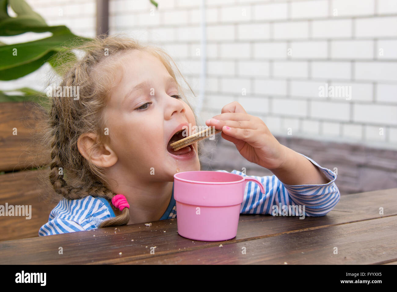 Quattro anni di ragazza cialde per mangiare e bere il tè al tavolo sulla veranda Foto Stock
