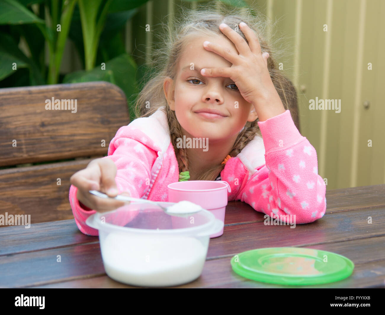 Sei anni di ragazza versa lo zucchero nel tè cucchiaio una piccola prima colazione sulla veranda Foto Stock