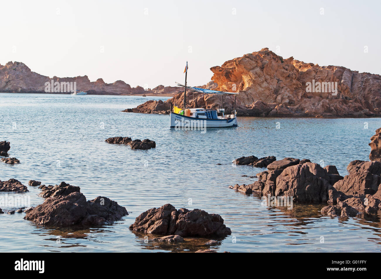 Menorca: barca da pesca a Cala Pregonda beach, isolata insenatura di scogli e sabbia rossa cercando come il pianeta di Marte Foto Stock