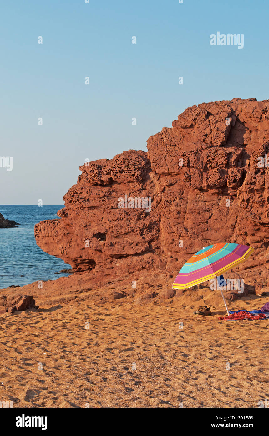 Minorca, Spagna: sabbia rossa e un ombrellone a Cala Pregonda beach, isolata insenatura con rocce, un paesaggio che sembra il pianeta di Marte Foto Stock