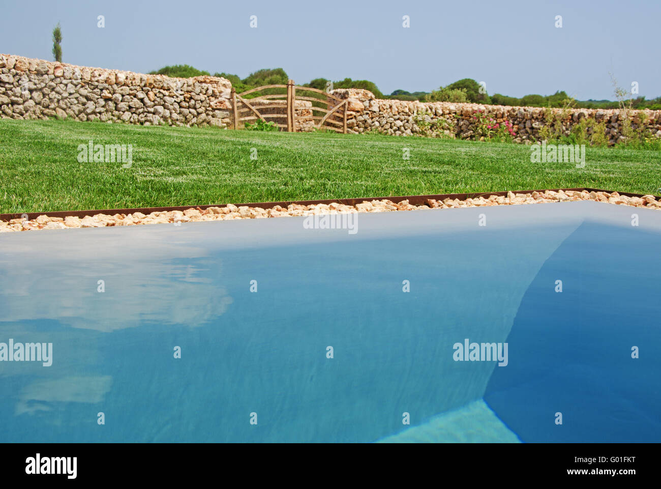 Minorca isole Baleari: un cancello in legno, prato, muro di pietra e la piscina riflessioni n la campagna meinorcan Foto Stock