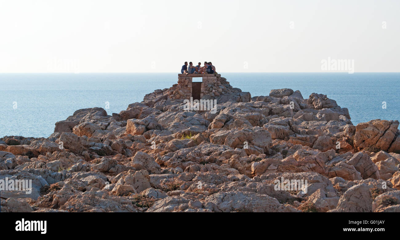 Minorca isole Baleari, Spagna, Europa: menorcan uomini in attesa per il tramonto su un edificio in pietra di Punta Nati faro Foto Stock