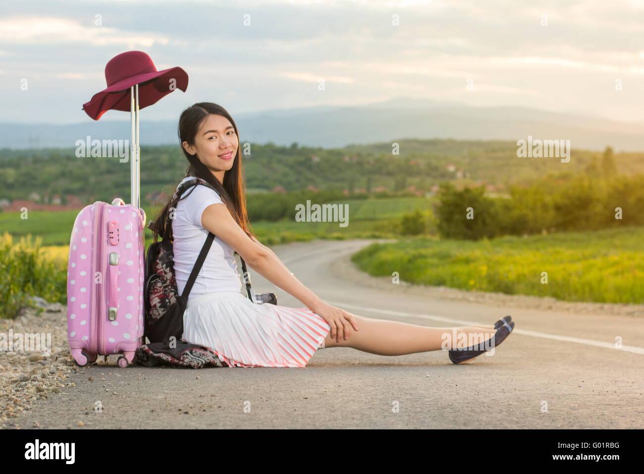 Lonely ragazza seduta sulla strada vicino alla sua valigia Foto Stock