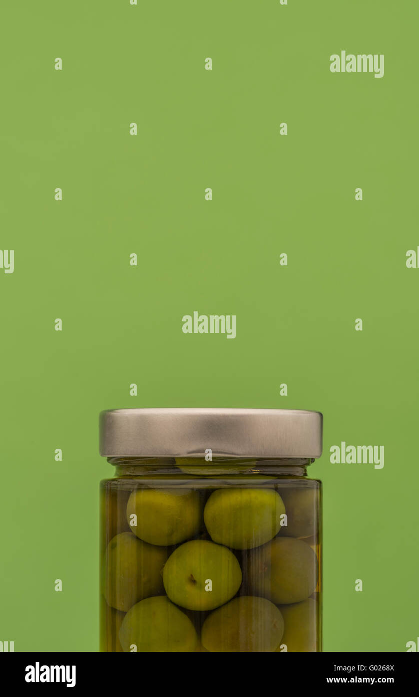 Vaso di olive verdi con coperchio color argento contro lo sfondo di colore verde Foto Stock