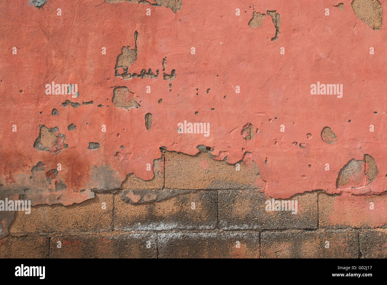 Il vecchio muro arancione con parti rotte. Mattoni di calcestruzzo nella base. Foto Stock