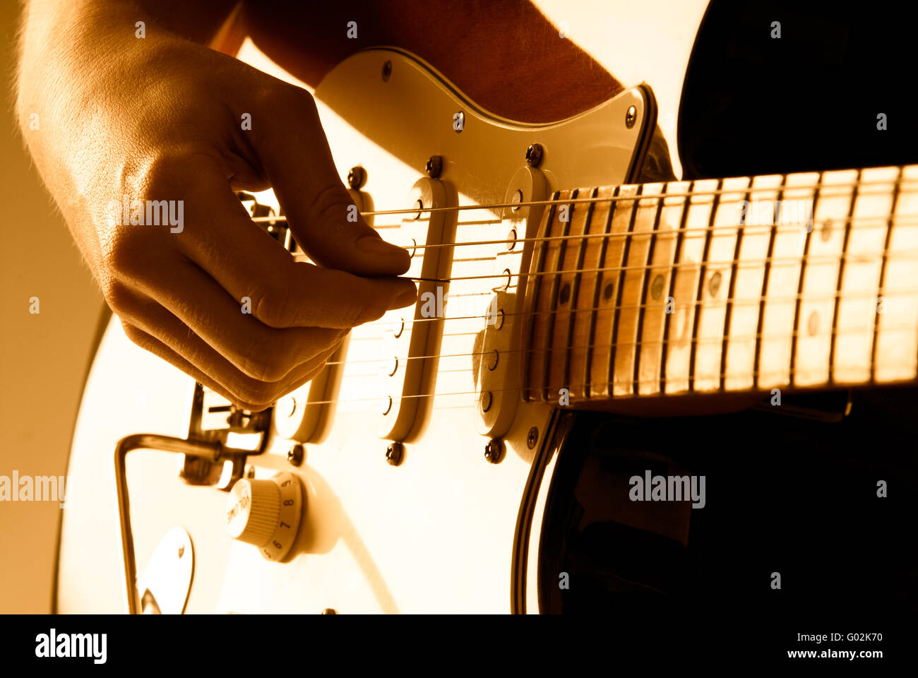 Raccolta a mano le corde di una chitarra con profondità di campo e illuminazione arancio. Foto Stock