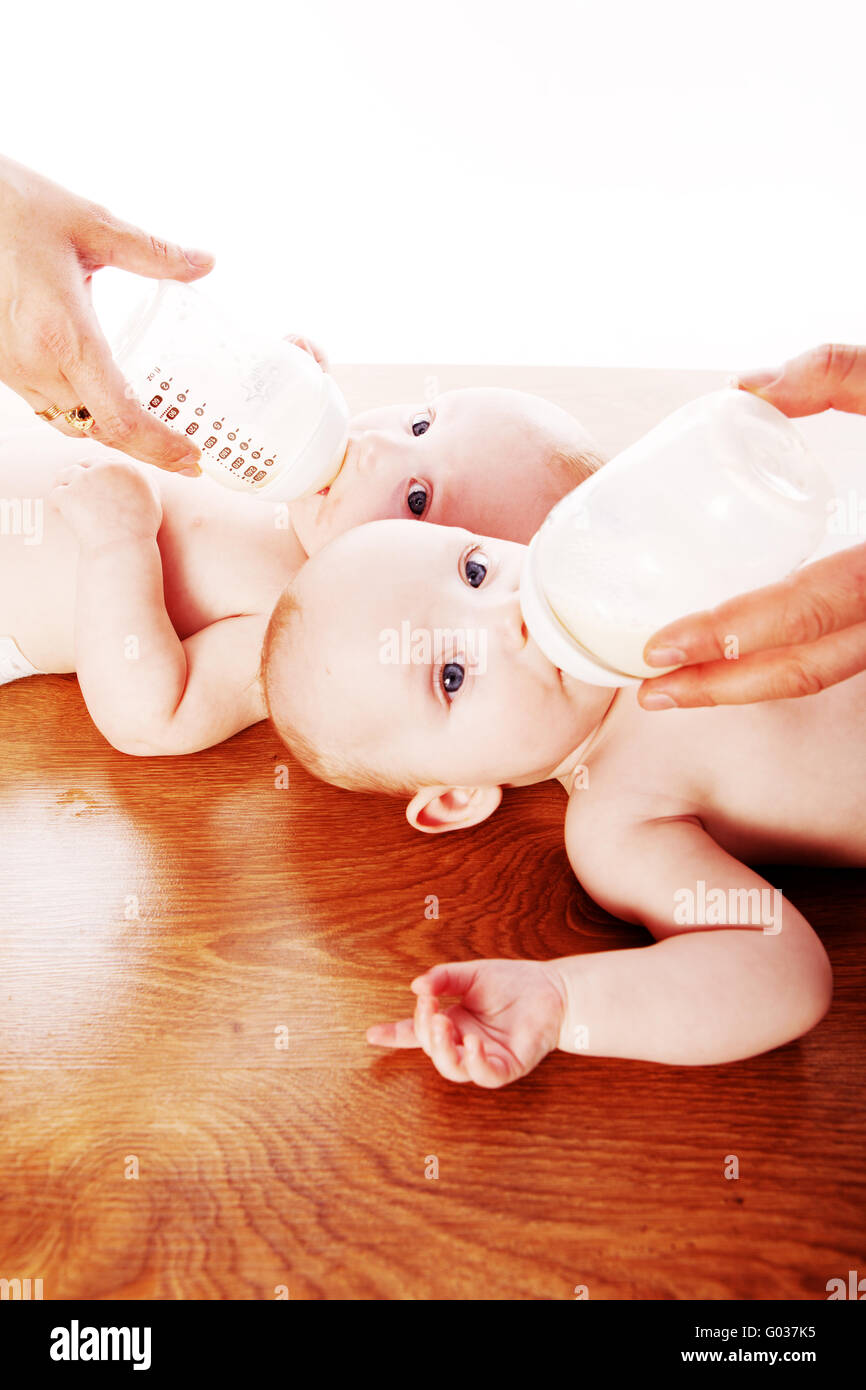 Baby gemelli di bere latte dalla bottiglia tenendo da parte dei loro genitori Foto Stock