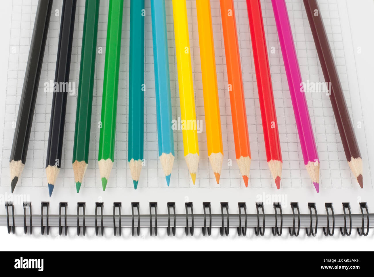 Matite multicolore su aperto il notebook a spirale Foto Stock
