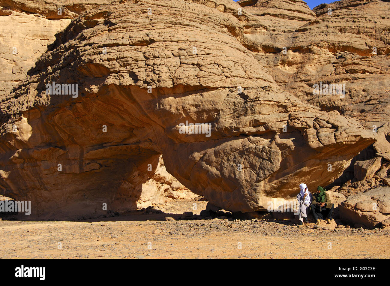 Bedouin uomini seduti su un arco di roccia, il deserto del Sahara Foto Stock